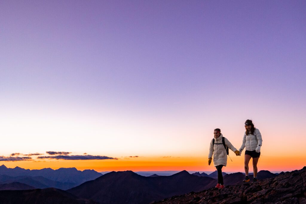 Two brides hiking off the summit of Handies Peak at sunset after their mountaintop elopement