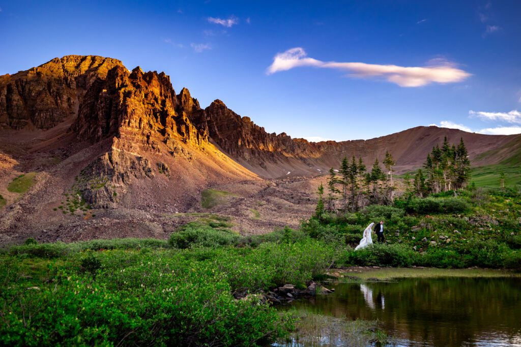 A bride and groom walking through an alpine meadow with Cathedral peak in the background at sunrise