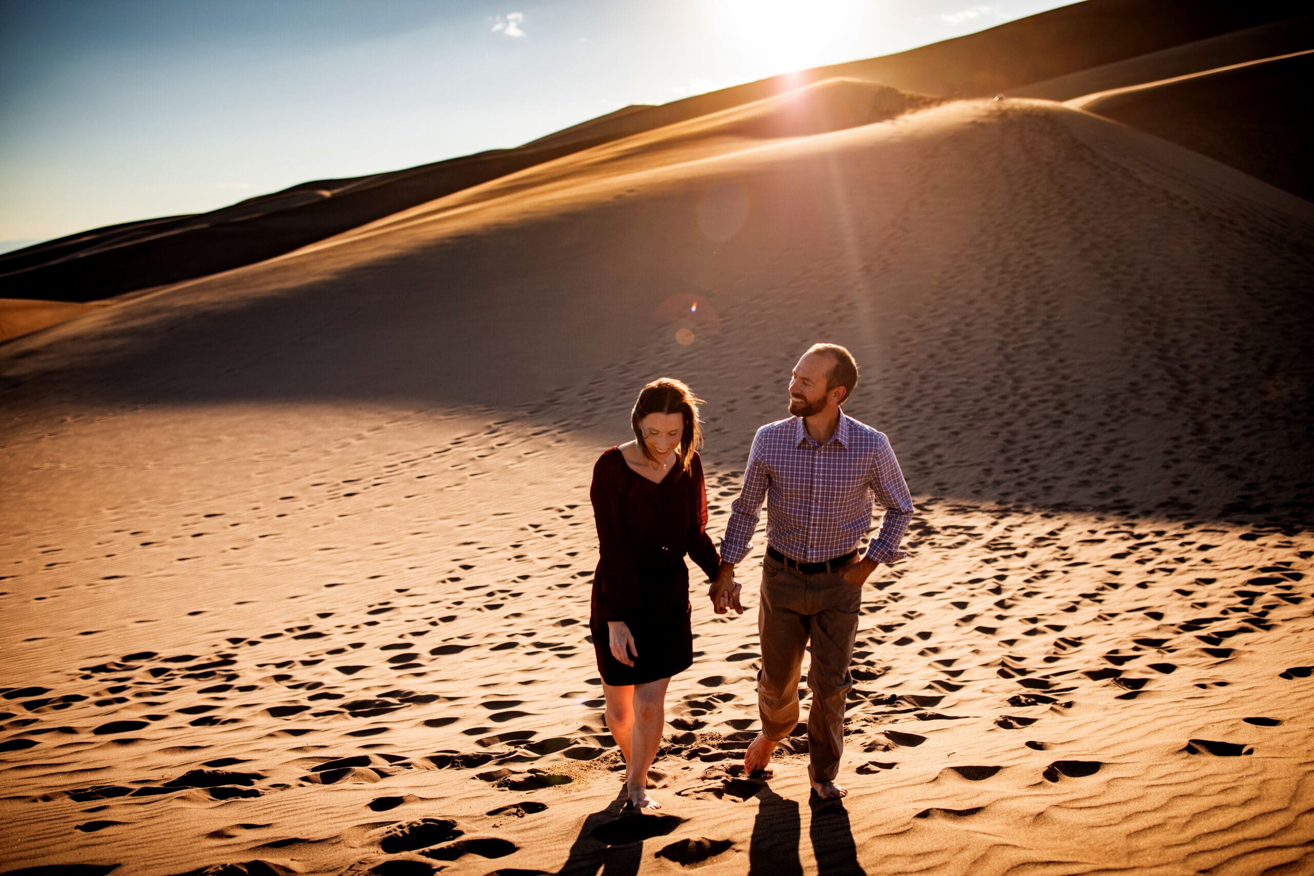 A couple walking hand in hand across the Sand Dunes in southern Colorado with the sun setting behind them