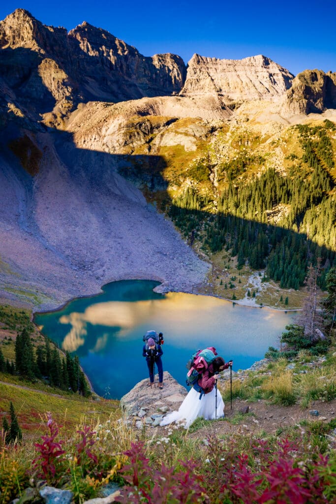 A bride and groom hiking out from the Lower Blue Lakes overlook with their hiking gear and wedding attire on