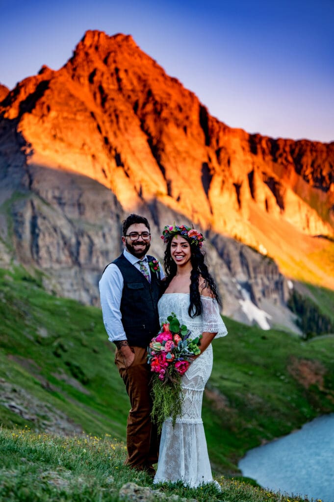 A bride and a groom looking at the camera smiling for a couple's portrait on their elopement day at Upper Blue Lakes in Ridgeway Colorado at Sunrise