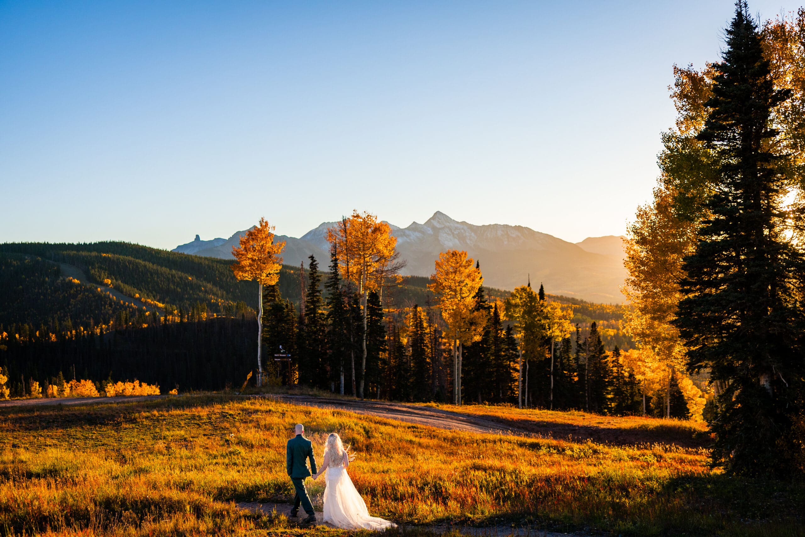 A bride and a groom holding hands walking in Telluride, Colorado at sunset as the sun dips behind Wilson Peak