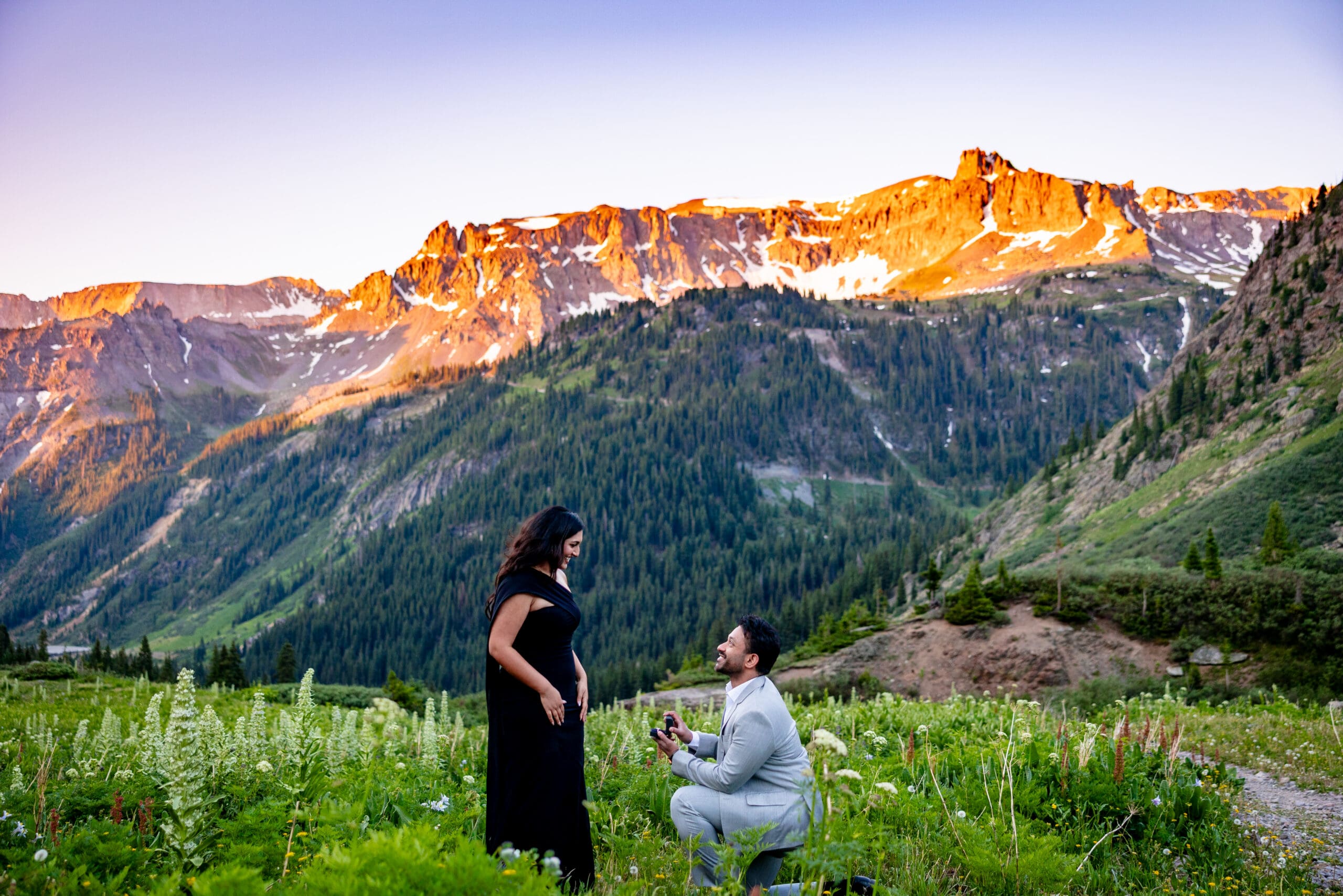 A man proposing to a woman in a mountain field at sunset during wildflower season