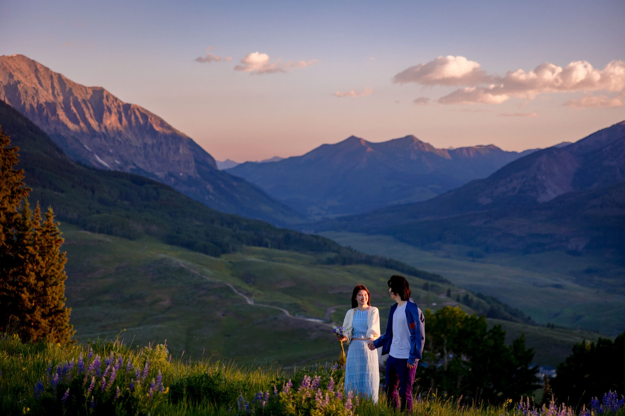 A couple at the top of Mt. Crested Butte near Ten Peaks wedding area at sunrise with Gothic Mountain and the Crested Butte valley behind them during wildflower season