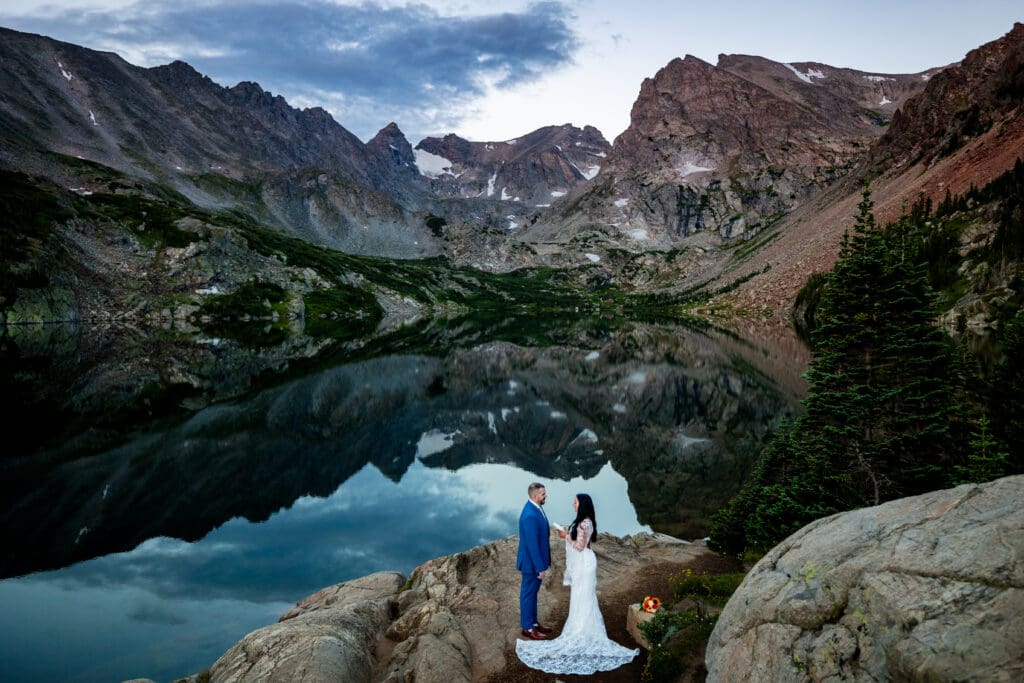 A bride and groom saying their vows to one another at Lake Isabelle at sunrise. The lake is a perfect reflection of the peaks behind the couple.